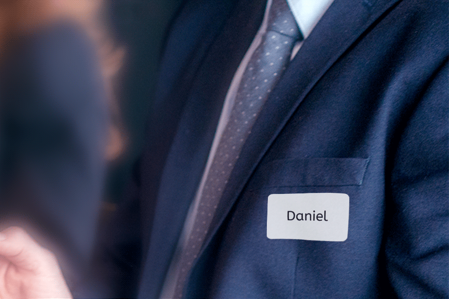 Un homme en costume porte un badge avec le nom "Daniel" sur le côté gauche de sa poitrine.