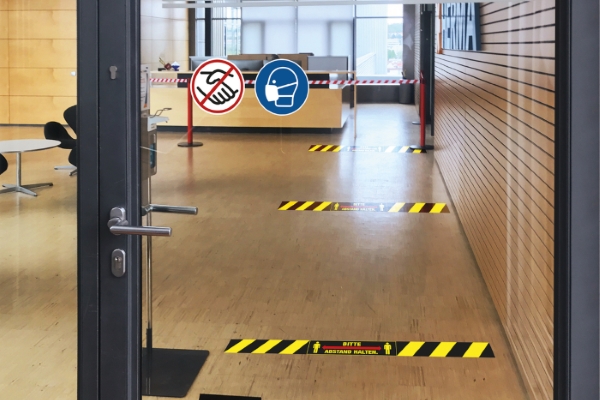 Translation: "Porte avec panneaux d'indication et autocollants au sol pour garder vos distances.