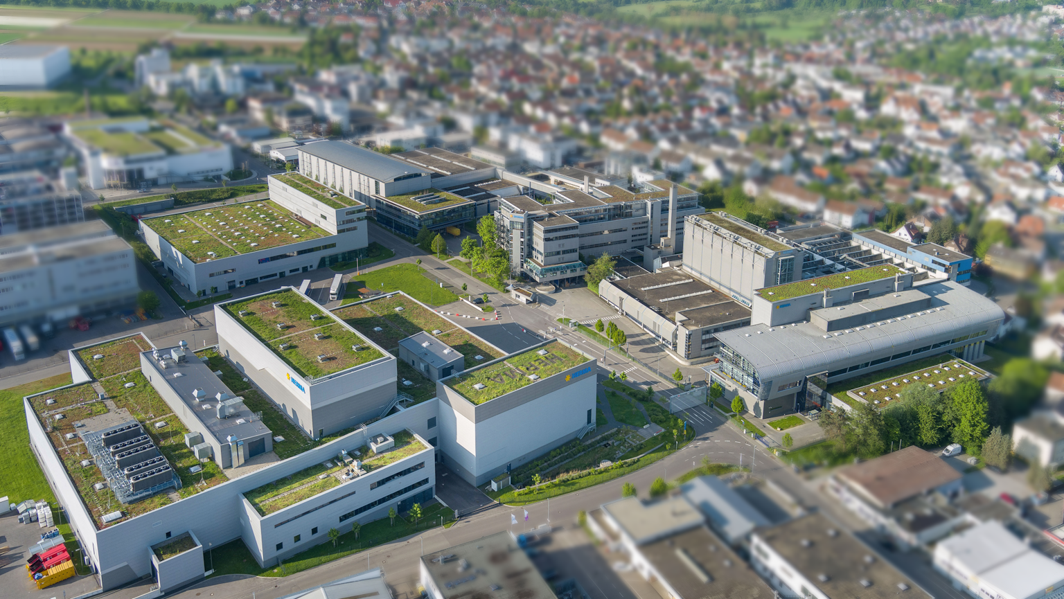 Vue aérienne d'une zone d'activités moderne avec plusieurs bâtiments et des toits végétalisés, entourée d'un paysage urbain.