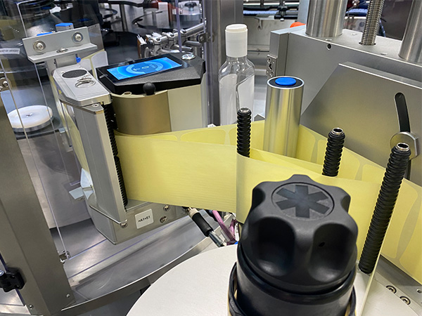 Un appareil d'étiquetage avec une étiquette jaune, qui est apposée sur des bouteilles, se trouve dans un environnement de production.