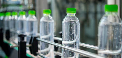 Des bouteilles d'eau avec des bouchons verts sur un tapis roulant dans une usine de production.