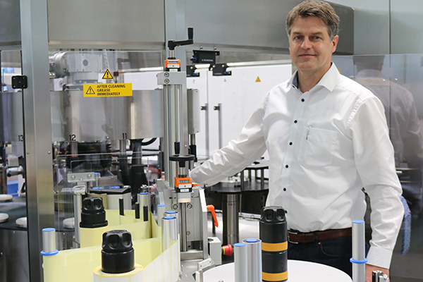 Un homme se tient à côté d'une machine industrielle pour le traitement des bouteilles, entouré de divers conteneurs et appareils techniques.