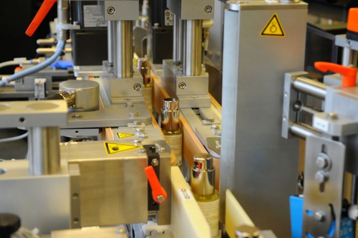 Machines automatisées pour le remplissage de bouteilles dans une ligne de production, avec divers composants mécaniques et étiquettes de sécurité.