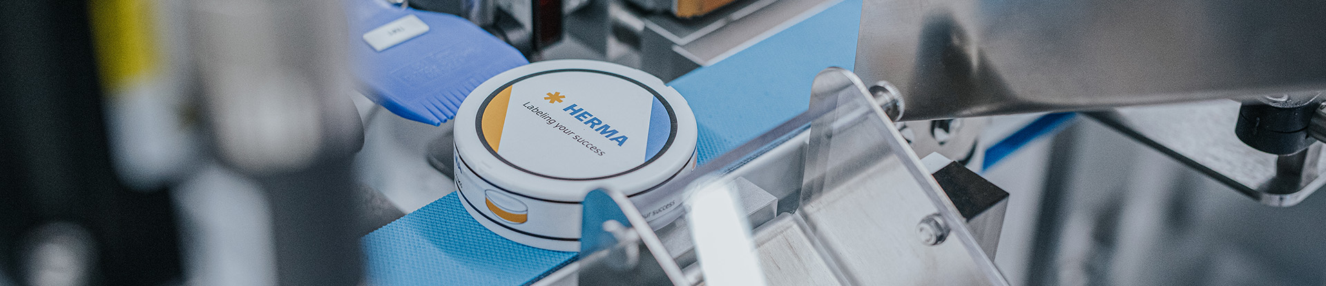 Une boîte avec le logo de 'HERMIA' sur un tapis roulant dans un environnement de production.