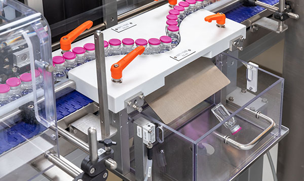 Machine d'emballage automatisée avec des flacons sur un tapis roulant et une boîte prête à être emballée.