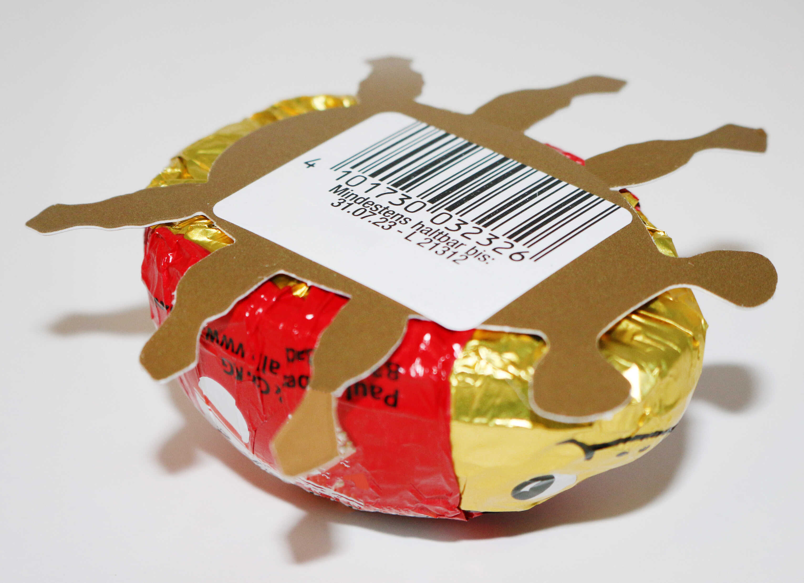 Bonbon rond en chocolat avec un emballage doré et rouge, décoré d'une figurine en carton en forme de soleil et d'un code-barres.