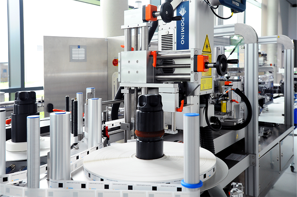 Une machine d'emballage automatisée avec des bouteilles sur un convoyeur, équipée de systèmes d'étiquetage et d'impression.