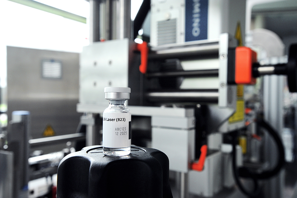 Une seringue contenant un liquide clair est posée sur un couvercle noir devant une machine industrielle.