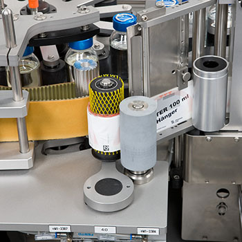 Machine d'étiquetage de bouteilles avec différents étiquettes et contenants dans un environnement industriel.