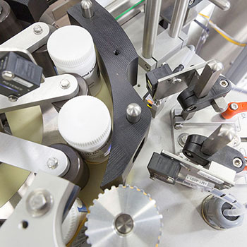 Machine à étiqueter des bouteilles, avec différents composants mécaniques et capteurs pour une manipulation précise.