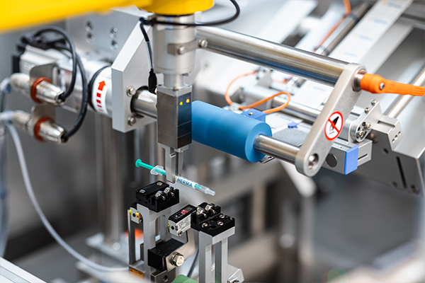 Machine automatisée avec un bras robotisé tenant une seringue, entourée de divers composants mécaniques et capteurs.