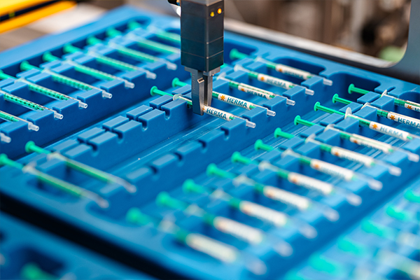 Un appareil automatisé prélève des seringues dans un conteneur bleu comportant plusieurs compartiments, conçu pour le stockage des seringues.