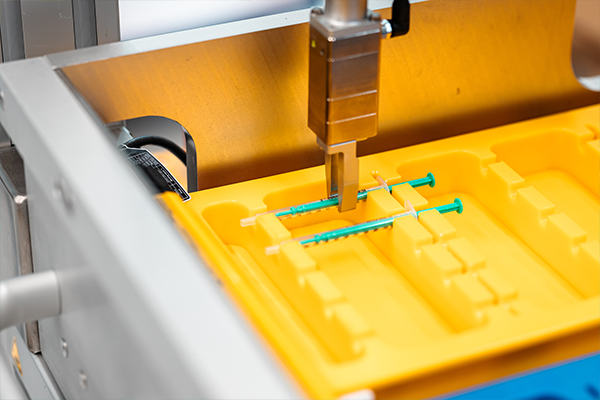 Une machine place des seringues vertes dans un support jaune, conçu pour le stockage ou le transport de dispositifs médicaux.