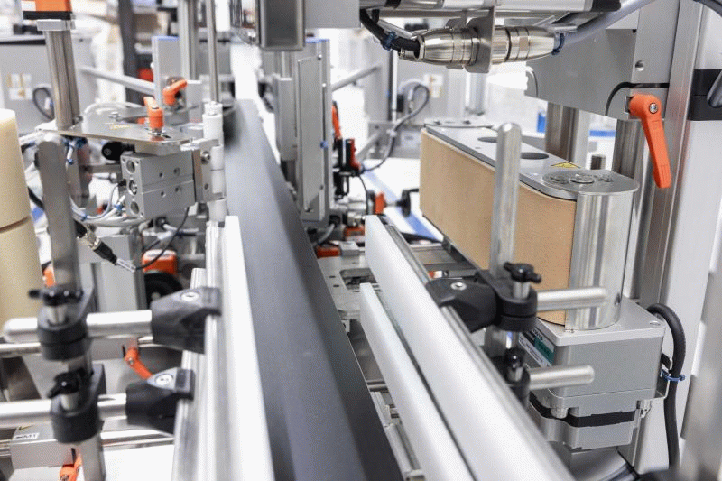 Machines automatisées pour l'emballage, avec des convoyeurs et divers composants mécaniques pour la manipulation des produits.