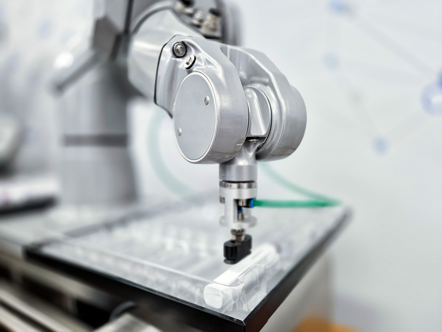 Bras de robot industriel avec pince, positionné sur une surface transparente, prêt à saisir un objet.