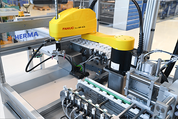 Un robot industriel avec un bras jaune qui travaille sur une machine automatisée pour assembler ou déplacer des composants.