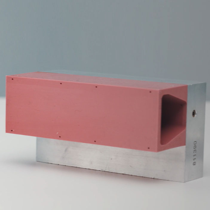 Un bloc rectangulaire avec un dessus rouge et un dessous métallique, avec une ouverture sur un côté.