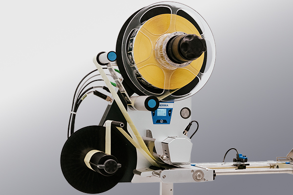 Un composant de machine avec une grande bobine de matériau jaune, relié par des tuyaux et un panneau de contrôle, destiné à la transformation ou à l'emballage.