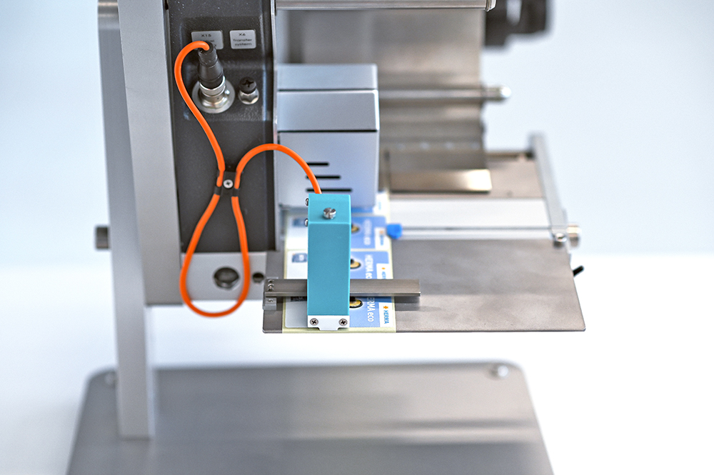 Un dispositif technique avec un composant bleu, monté sur une plaque métallique, relié par un câble orange.