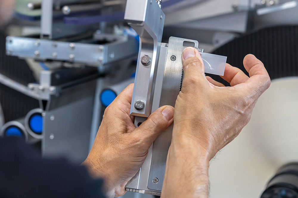 Une personne ajuste un instrument de mesure précis avec les deux mains, tout en travaillant sur une machine technique.