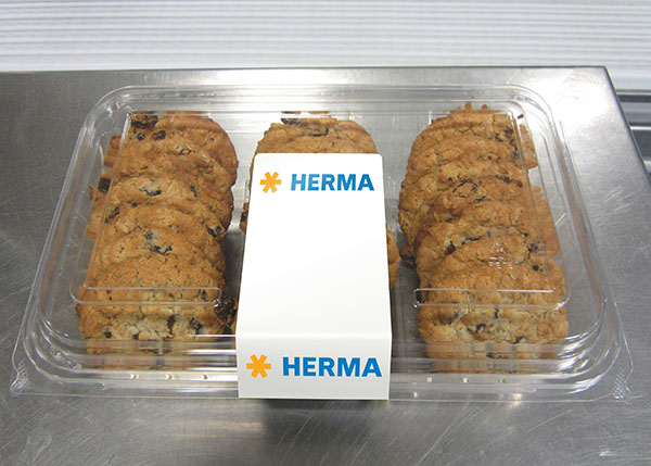 Un emballage transparent contenant plusieurs biscuits au chocolat, au centre avec une étiquette blanche portant l'inscription 'HERMA'.
