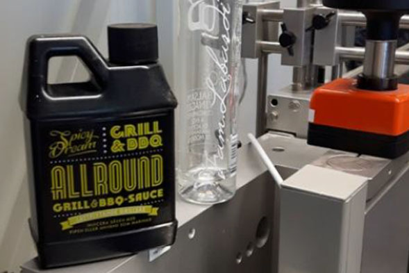 Une bouteille de sauce barbecue et un verre transparent sont posés sur une machine dans un environnement de production.