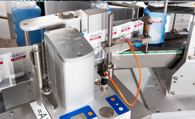 Machine d'étiquetage de bouteilles avec des mécanismes de contrôle précis et des affichages numériques. Des bouteilles de différentes couleurs sont visibles.