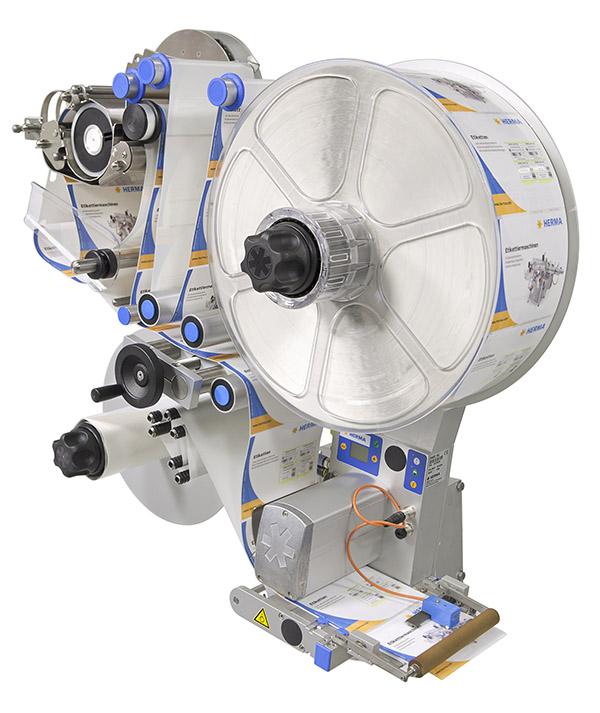 Machine à étiqueter avec un grand rouleau d'étiquettes, différents éléments de commande et un mécanisme de sortie.