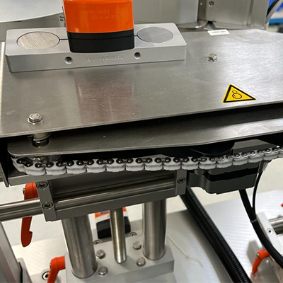 Un composant de machine avec un élément orange, des surfaces métalliques et un entraînement par chaîne, monté dans un environnement industriel.