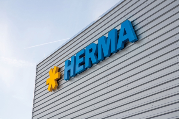 Le logo de l'entreprise HERMA en lettres bleues avec une étoile jaune sur un mur gris.