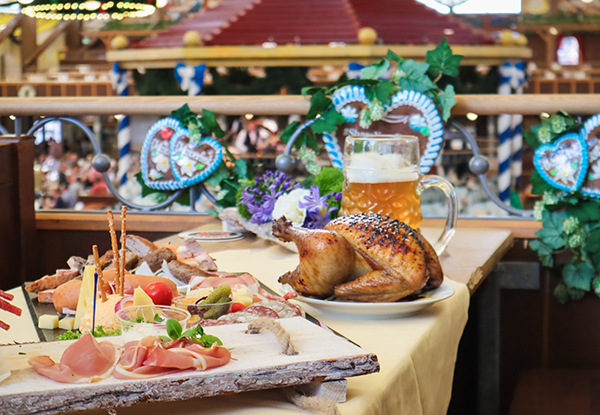 Un table avec une sélection de charcuterie, de fromage et de légumes, accompagnée d'un poulet rôti et d'un grand verre de bière dans une ambiance festive.