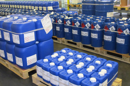Étiquettes GHS et étiquettes chimiques sur des bidons en plastique bleus, sur des palettes.