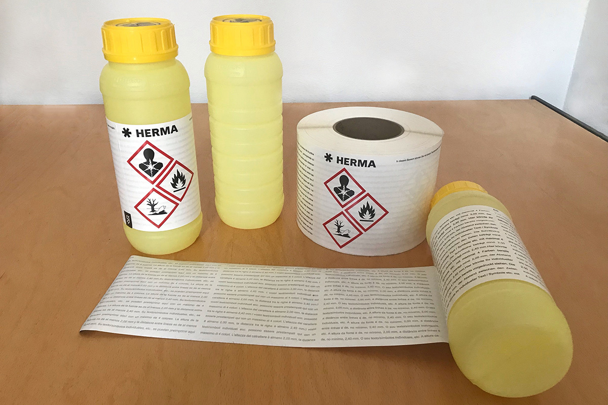 Deux bouteilles jaunes avec des symboles de danger et un rouleau d'étiquettes sur une table. Les étiquettes contiennent des informations de sécurité.