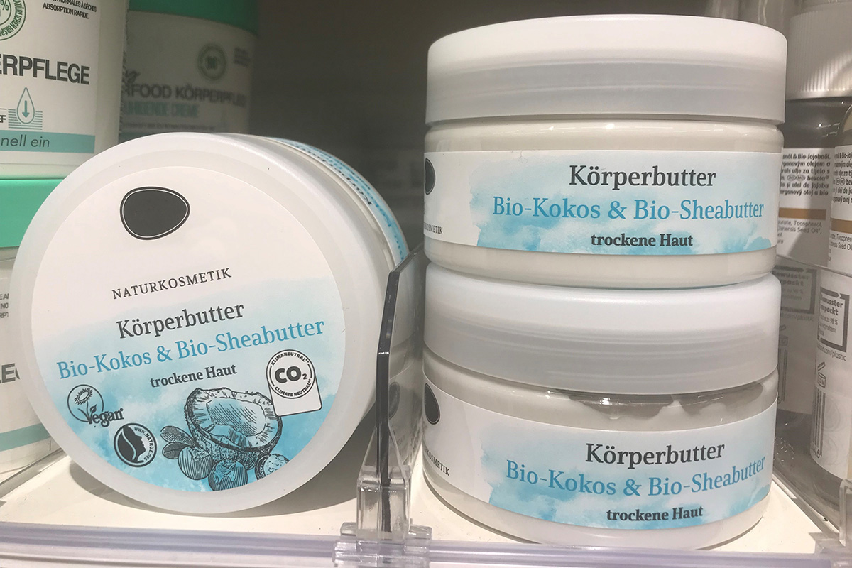 Pot de crème blanche avec du beurre corporel en cosmétique naturelle sur l'étagère, étiqueté sur le couvercle et le corps avec des étiquettes imprimées en bleu et blanc.