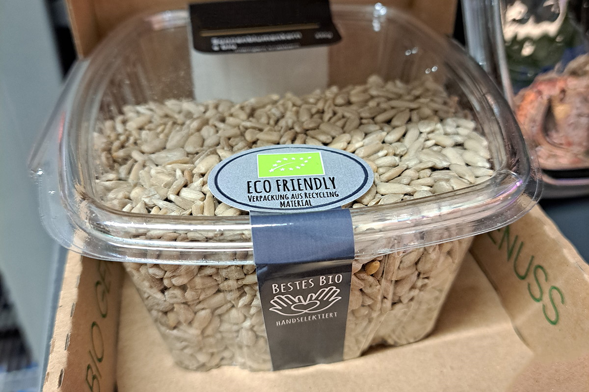 Solutions alimentaires : Étiquette produit et de fermeture deux-en-un, imprimée en couleur, qui relie le couvercle et le corps d'un emballage en clamshell contenant des noix.