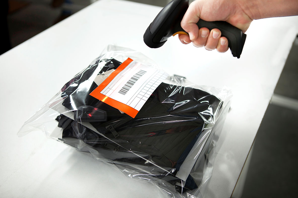 Étiquettes à codes-barres : Étiquette à code-barres sur emballage en film dans la zone de préparation des commandes, avec scanner manuel.