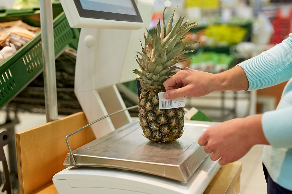 Étiquetage des aliments : balance pour fruits et légumes au supermarché, une femme colle une étiquette alimentaire sur une ananas.