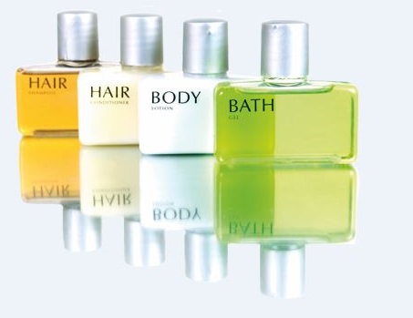 Quatre bouteilles de produits de soin : shampooing, après-shampooing, lotion pour le corps et gel douche, disposées sur une surface réfléchissante.