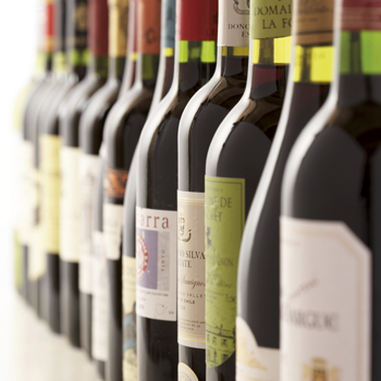 Une rangée de bouteilles de vin avec différentes étiquettes, disposées sur une table. Les bouteilles sont agencées dans des couleurs et des formes variées.