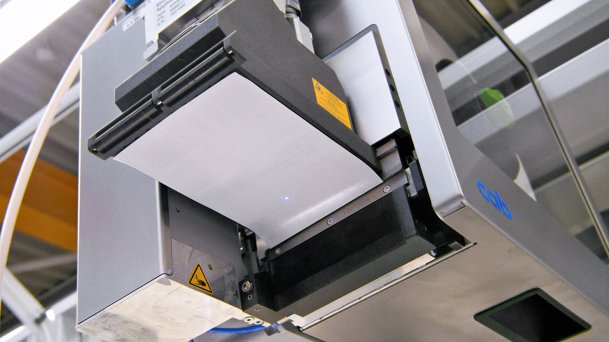 Un imprimante avec une unité d'impression vide, prête à imprimer. La machine présente des composants techniques et des étiquettes de sécurité.