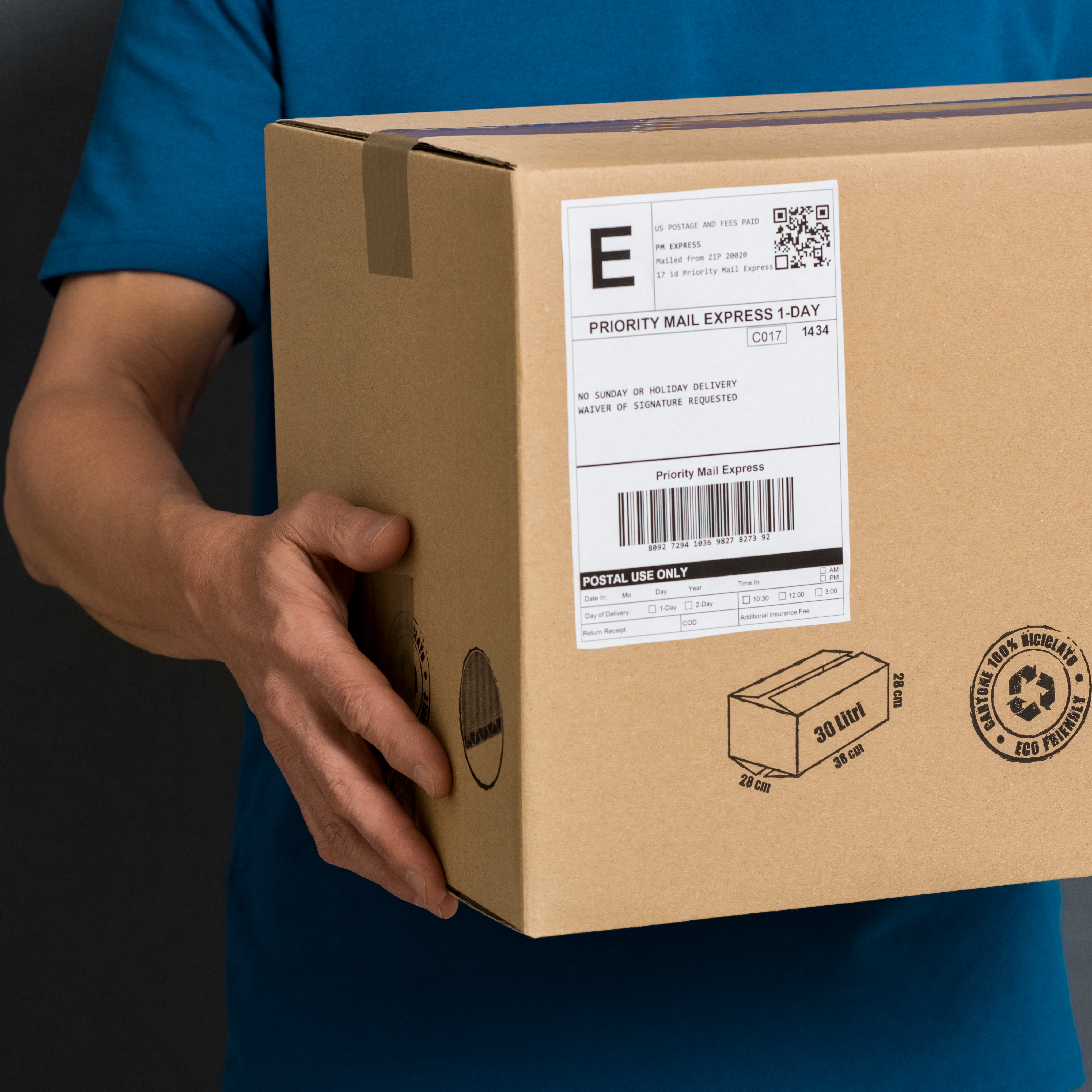 Une personne tient un colis marron avec une étiquette d'expédition indiquant "Priority Mail Express".
