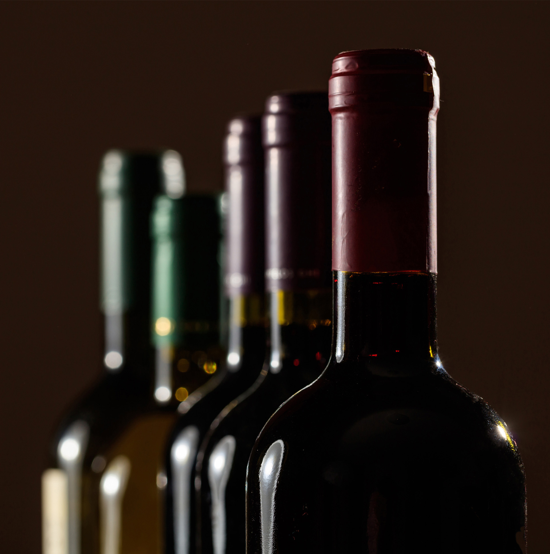 Cinq bouteilles de vin avec des couleurs de bouchon différentes sont alignées, partiellement floues en arrière-plan.