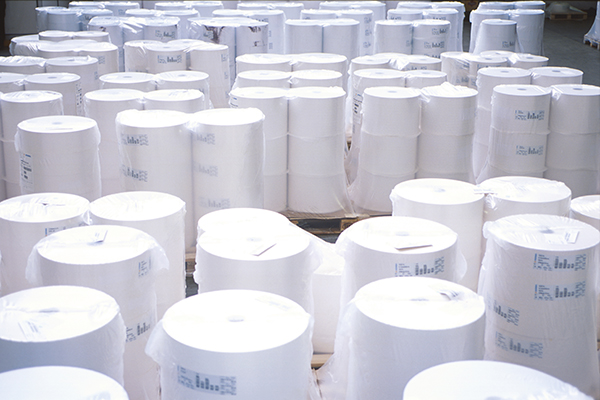 Des rouleaux de papier, soigneusement empilés dans un entrepôt, entourés d'autres rouleaux de papier.