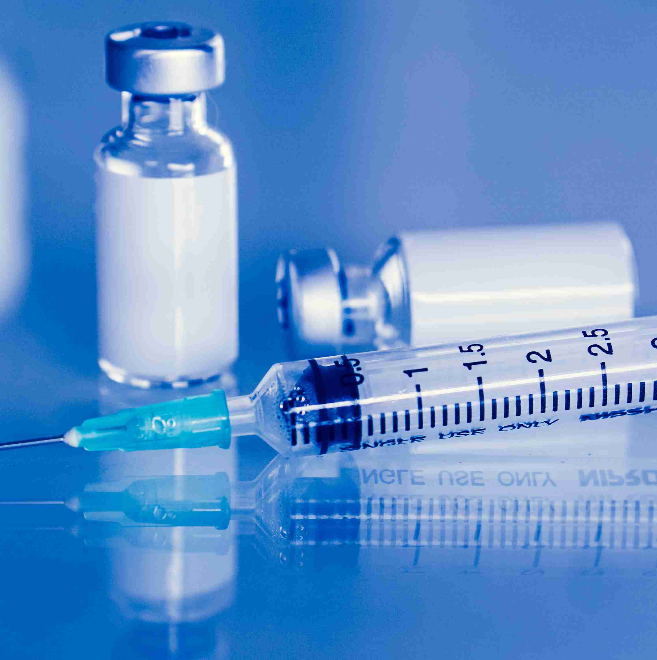 Une seringue avec une aiguille et deux flacons en verre contenant un liquide clair sur un fond réfléchissant.