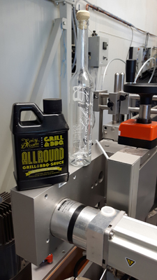 Une bouteille et une bouteille de sauce pour grillades et barbecue sont posées sur une surface de machine dans un environnement de production.