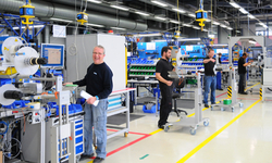 Des ouvriers dans un atelier de production, qui se tiennent devant des machines et à leurs postes de travail tout en effectuant diverses tâches.