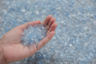 Une main tient une multitude de particules en plastique bleu transparent, entourées d'autres particules similaires sur une surface.