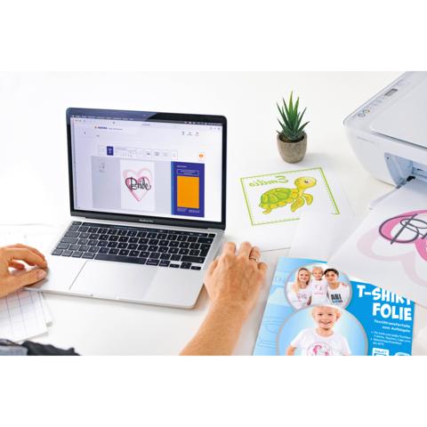 Eine Person arbeitet an einem Laptop, um ein Design für T-Shirt-Folie zu erstellen. Neben dem Laptop liegen verschiedene Druckmaterialien.