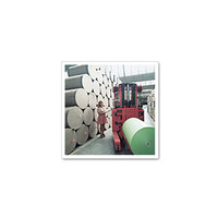 Une femme manœuvre un chariot élévateur dans un entrepôt pour déplacer de grands rouleaux de papier, tandis que d'autres rouleaux sont empilés en arrière-plan.