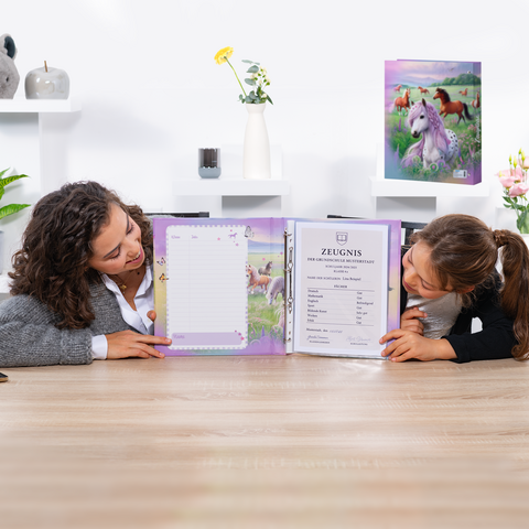 Deux filles sont assises à la table et regardent un bulletin scolaire ouvert dans un classeur coloré avec un motif de licorne.